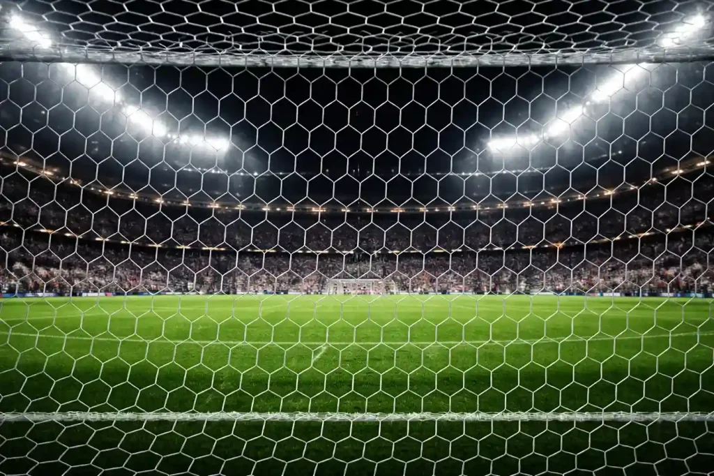 Aficionados en la grada de un estadio de fútbol viendo un partido nocturno bajo focos
