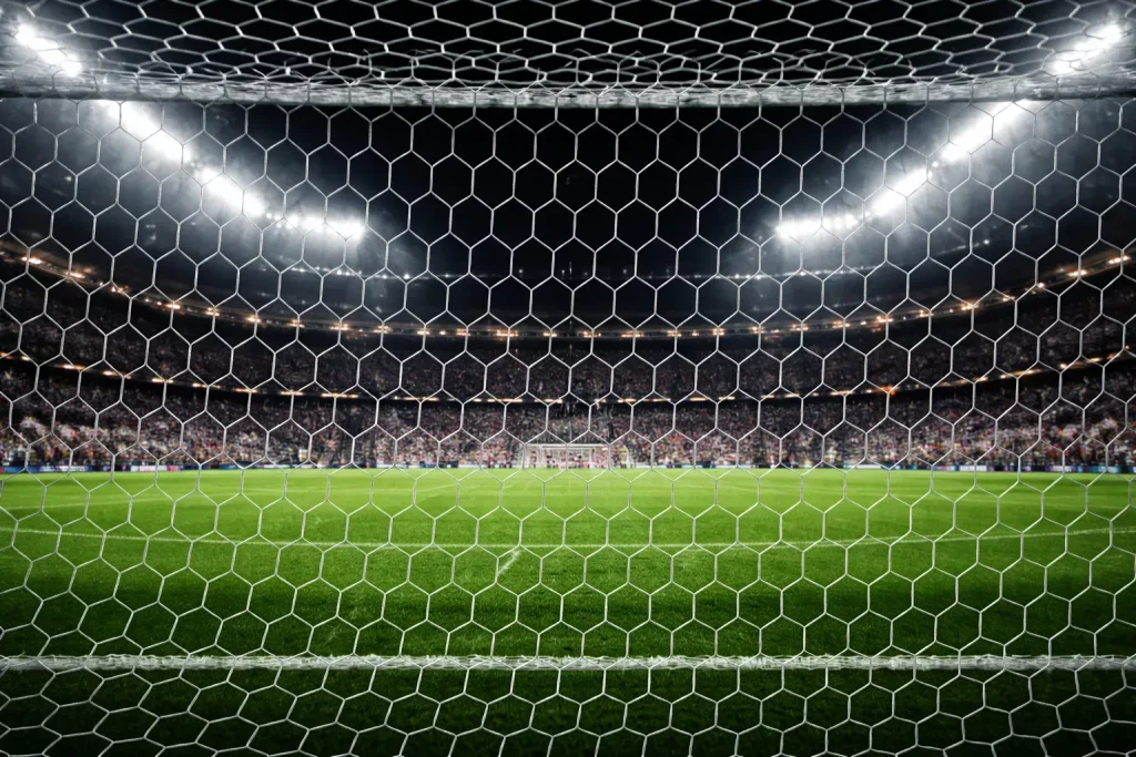 Aficionados en la grada de un estadio de fútbol viendo un partido nocturno bajo focos
