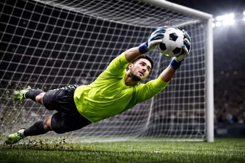 Portero de fútbol atrapando el balón en una estirada bajo la luz del estadio